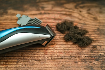  Side on view of a set of electric hair clippers, human hair and a grader attachment on the wooden floor of a hair salon with intentional elective focus and shallow depth of field