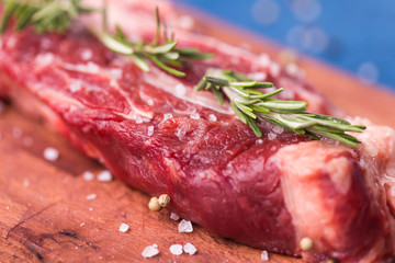 Raw meat. A large piece of beef chop on a wooden cutting board with rosemary and spices, close-up.