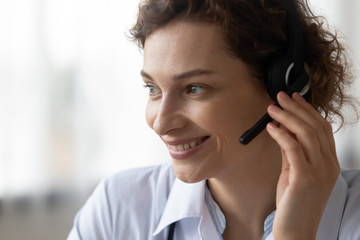 Close up head shot of smiling female young doctor operator wearing headset with microphone looking...