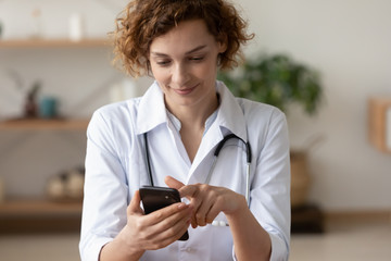 Young female physician using mobile healthcare tech app consulting remote patient online in telemedicine software. Woman doctor therapist holding smart phone texting message for digital consultation.