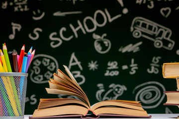 Back to school background with books, pencils and globe on white table on a green blackboard background.