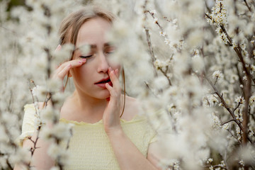 Young girl blowing nose and sneezing in tissue in front of blooming tree. Seasonal allergens...