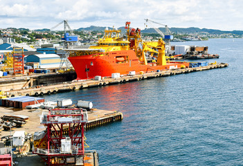 A large orange and yellow colored Offshore Construction Vessel (OCV) is in a dry dock of a shipyard and is being repaired 