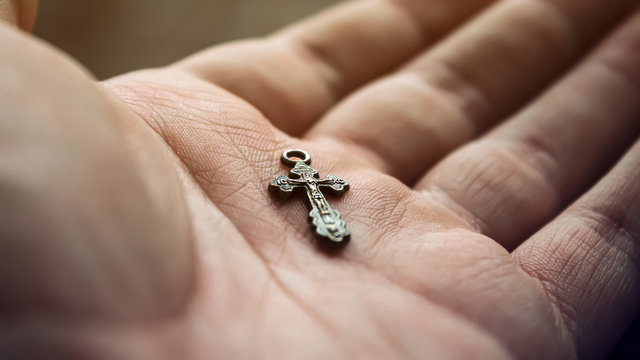 a small Christian cross on the palm of a man close-up. man holds out his hand, on which lies the symbol of religion. Orthodoxy in the hand. The concept of faith in the hands of mankind.