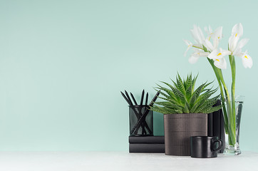 Fresh spring business workplace  - black stationery, books, coffee cup, green aloe in pot, white flowers in vase on green mint menthe wall and white wood desk.