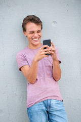Fototapeta premium smiling young man leaning against wall looking at cellphone