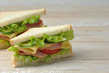 Sandwich with ham and cheese made of white bread. Light wooden background. Free space for text.