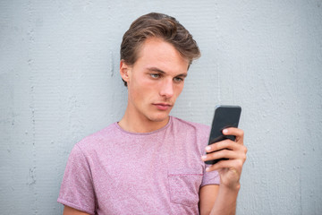 Close up serious young man leaning against wall looking at cellphone