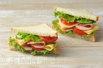 Ham and cheese sandwich on a light wooden background. Slices of fresh cucumber, tomato and salad are part of the sandwich filling. Close-up.