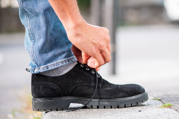 man hand tying shoelace on sidewalk