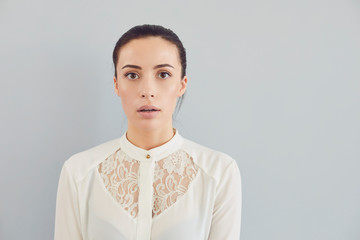 Puzzled insecure woman in white shirt on a gray background. Expression of emotion