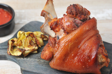Baked pork  knuckle on a wooden board.  Ketchup sauce and grilled vegetables.  Wood background.  Close-up. Macro shot.