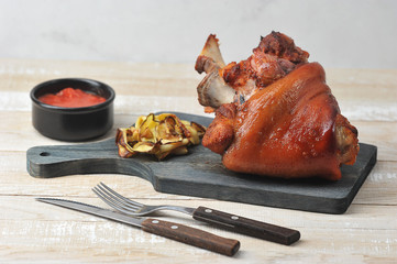 Baked pork  knuckle on a wooden board.  Ketchup sauce and grilled vegetables.  Wood background.  Close-up.