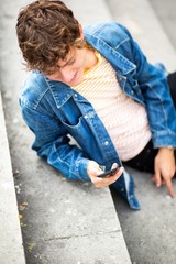 above happy young man sitting outside on steps looking at mobile phone