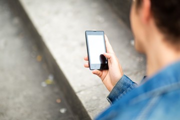 behind young man sitting outside holding mobile phone and looking at screen
