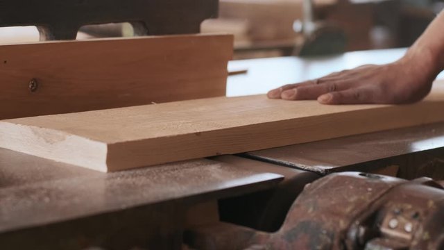 Woodwork and furniture making concept. Carpenter in the workshop handles the edge of the wooden parts on the machine plane close up
