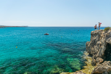 CYPRUS, NISSI BEACH - MAY 12/2018: tourists have fun and jump from a cliff into the azure sea.