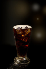 Glass cola with ice on a black background a glass of  cola in a popular bar. Pint of foamy drink in a restaurant