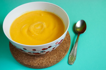 yellow soup - mashed pumpkin, potatoes, carrots, onions and cream in a white plate on a light blue background with a metal spoon on a brown stand . For lunch and dinner . Food for children