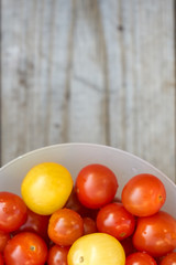 Yellow and red cherry tomatoes in a white bowl on a wooden table. Photo with copy space.