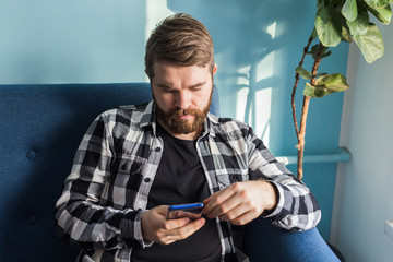 Technologies and leisure concept - Cheerful man sitting on the couch using his smartphone at home in the living room.