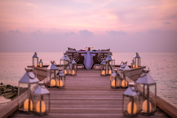 Romantic dinner on the beach with sunset, candles with palm leaves and sunset sky and sea. Amazing view, honeymoon or anniversary dinner landscape. Exotic island evening horizon, romance for a couple 