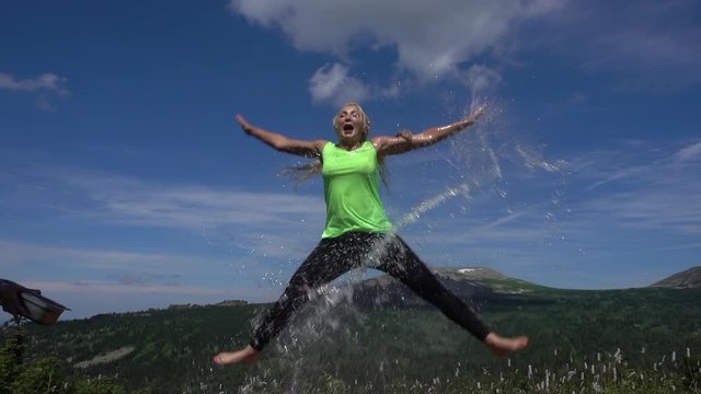 a young woman in a jump with a splash of water. athletic girl jumps up with flying jets of water against the background of summer mountains and sky. Sports and healthy lifestyle. Pretty fit girl