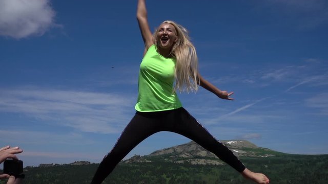 a happy young woman in leggings and a bright green t shirt jumps beautifully in the air against the background of a mountain valley. outdoor fitness, Sports and healthy lifestyle. Pretty fit girl