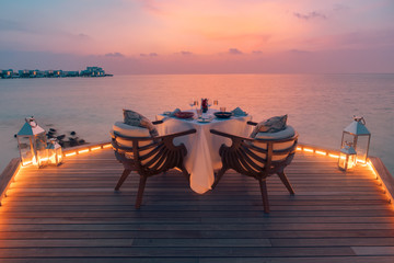 Romantic dinner on the beach with sunset, candles with elegant table, sunset sky and sea. Amazing honeymoon and anniversary couple destination. Romance and love background