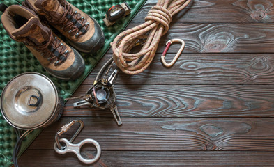 climbing equipment: rope, flashlight, trekking shoes, carabiners, burner, saucepan, tourist rug and other set on dark wooden background, top view. Travel concept.