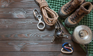 climbing equipment: rope, trekking shoes, carabiners, burner, saucepan, tourist rug and other set on dark wooden background, top view.
