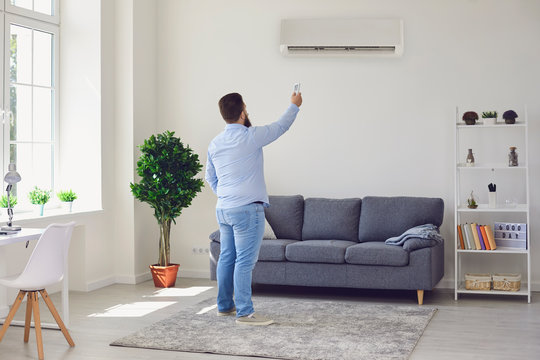 Fat funny man holding an air conditioning control panel while standing at home.