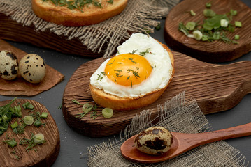 Breakfast eggs on bun, quail eggs, greens on a wooden plate.