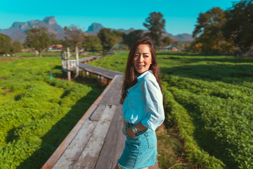 traveler asian girl posing smile in wear shirt and skirt jeans  on the walkway wood bridge with a outdoor nature a flower in sunlight in travel relaxing time concept
