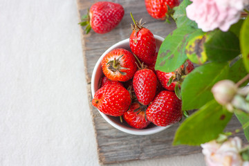 Fruit bowl full of fresh, red, jucy strawberries on wooden table. Pastel-colored decoration with a floral  arrangement with space for text. Top view.