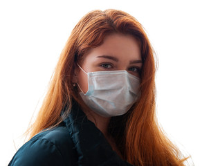 Horizontal shot of ill redhead girl wears medical mask to protect from catching disease, in black jacket, stands outdoor, suffers from epidemic illness, isolated background
