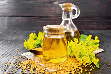 Oil mustard in jar and decanter with flower on wooden board