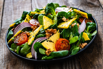 Fresh salad - blue cheese, cherry tomatoes, vegetables and walnuts on wooden background
