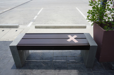 A cross tapes affixed on a bench showing available for one person. It's a sign of social distancing during Corona Virus (Covid 19) pandemic in public area. 