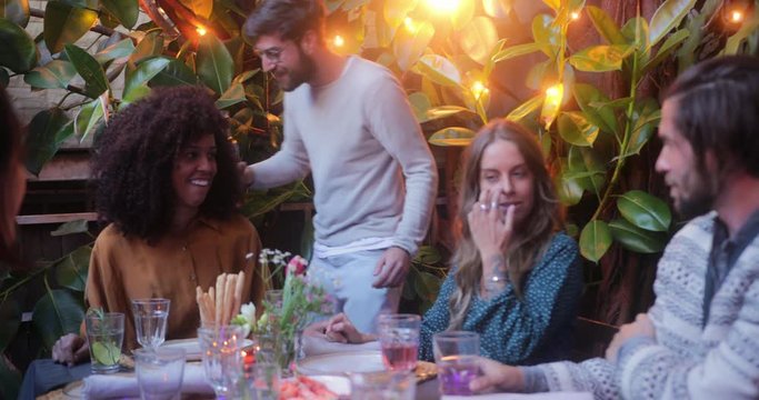 Man serving wine to multi-ethnic friends during meal on patio