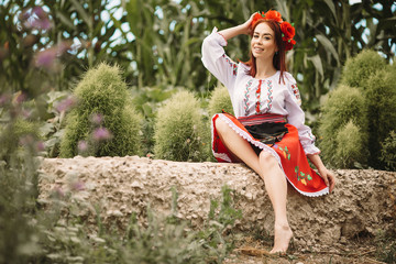 
Young  redhead moldavian girl dressed in traditional costume sitting on a stone against the...