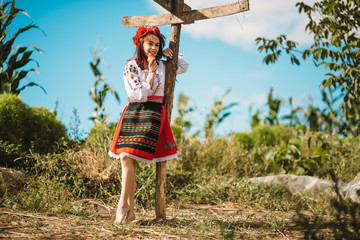 Young  redhead moldavian girl dressed in traditional costume staing near old pole with derections.