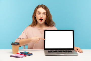 Amazed astonished woman, office employee, sitting at workplace and pointing empty laptop screen,...