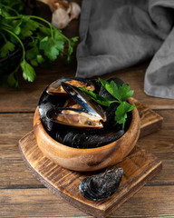 Raw mussels in a brown wooden plate on a brown wooden table