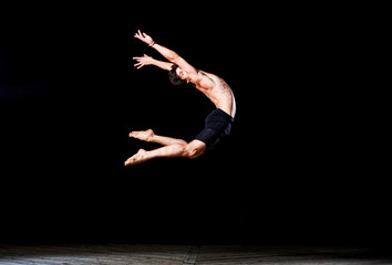 Modern ballet style male dancer performs on high lighted stage .