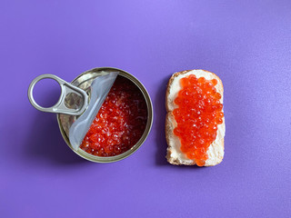 Sandwich with butter and red salmon caviar. Toast white bread is spread with butter or soft cheese. Violet monophonic background for backgrounds.