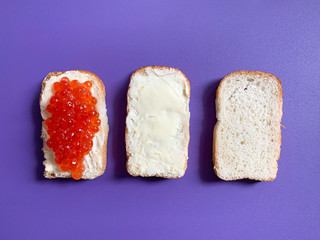 Sandwich with butter and red salmon caviar. Toast white bread is spread with butter or soft cheese. Violet monophonic background for backgrounds.