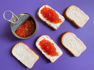 Sandwich with butter and red salmon caviar. Toast white bread is spread with butter or soft cheese. Violet monophonic background for backgrounds.
