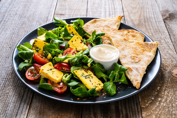 Fresh salad - blue cheese, cherry tomatoes, vegetables and homemade bread on wooden background 