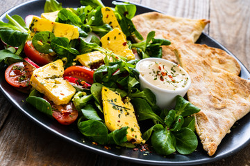 Fresh salad - blue cheese, cherry tomatoes, vegetables and homemade bread on wooden background 